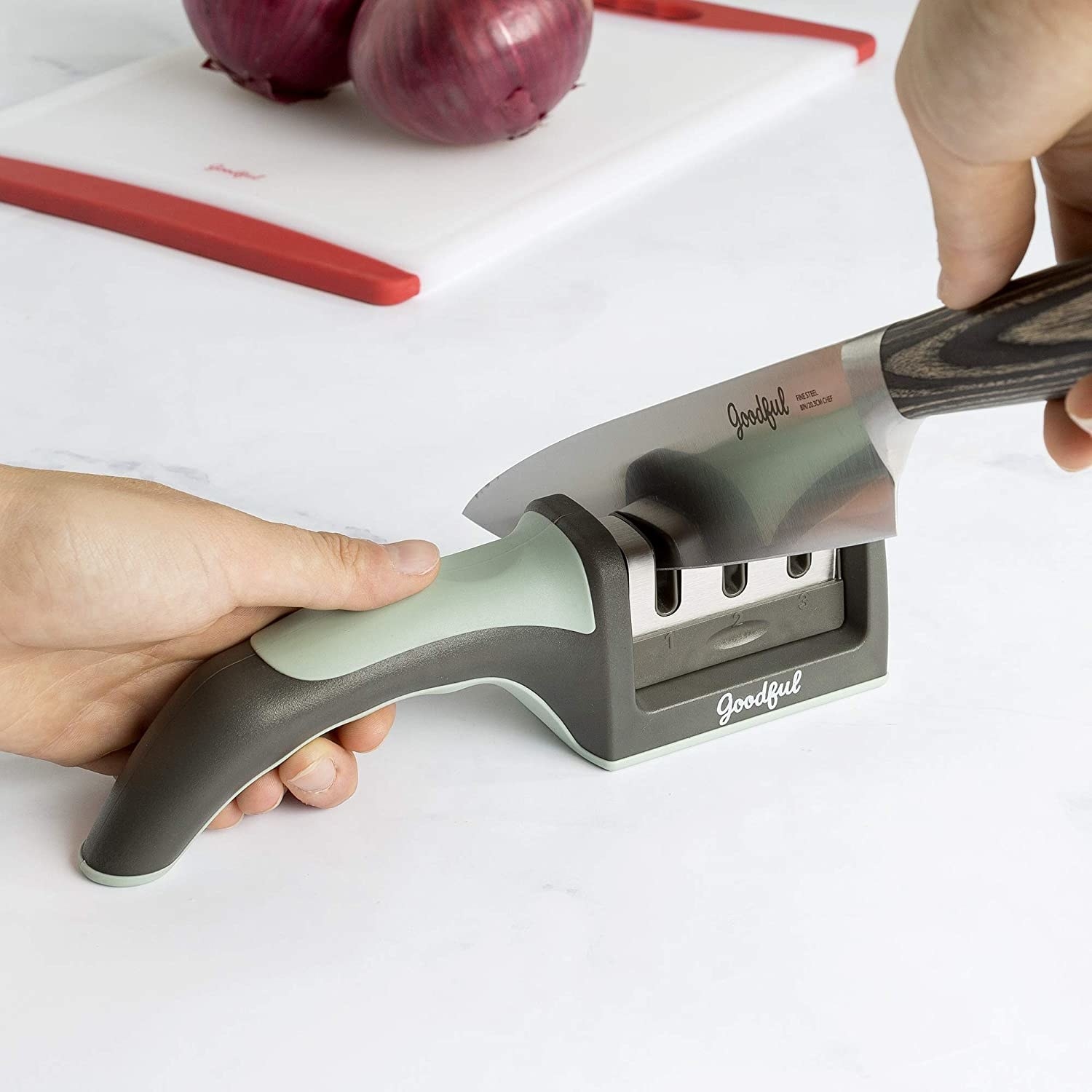 Hand uses green Goodful knife sharpener to sharpen large silver knife