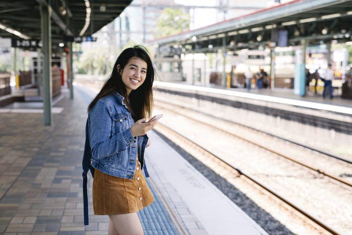 Young person standing on a train platform with their phone and smiling at the camera