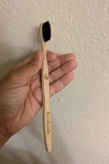 A reviewer photo of a hand holding a bamboo toothbrush with black bristles engraved with the number one 