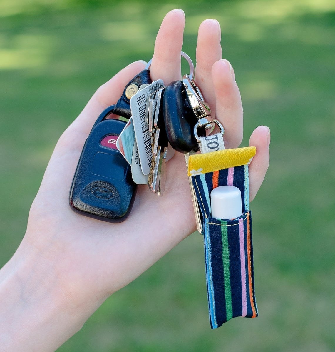 A person holding a keychain with the lip balm pouch on it