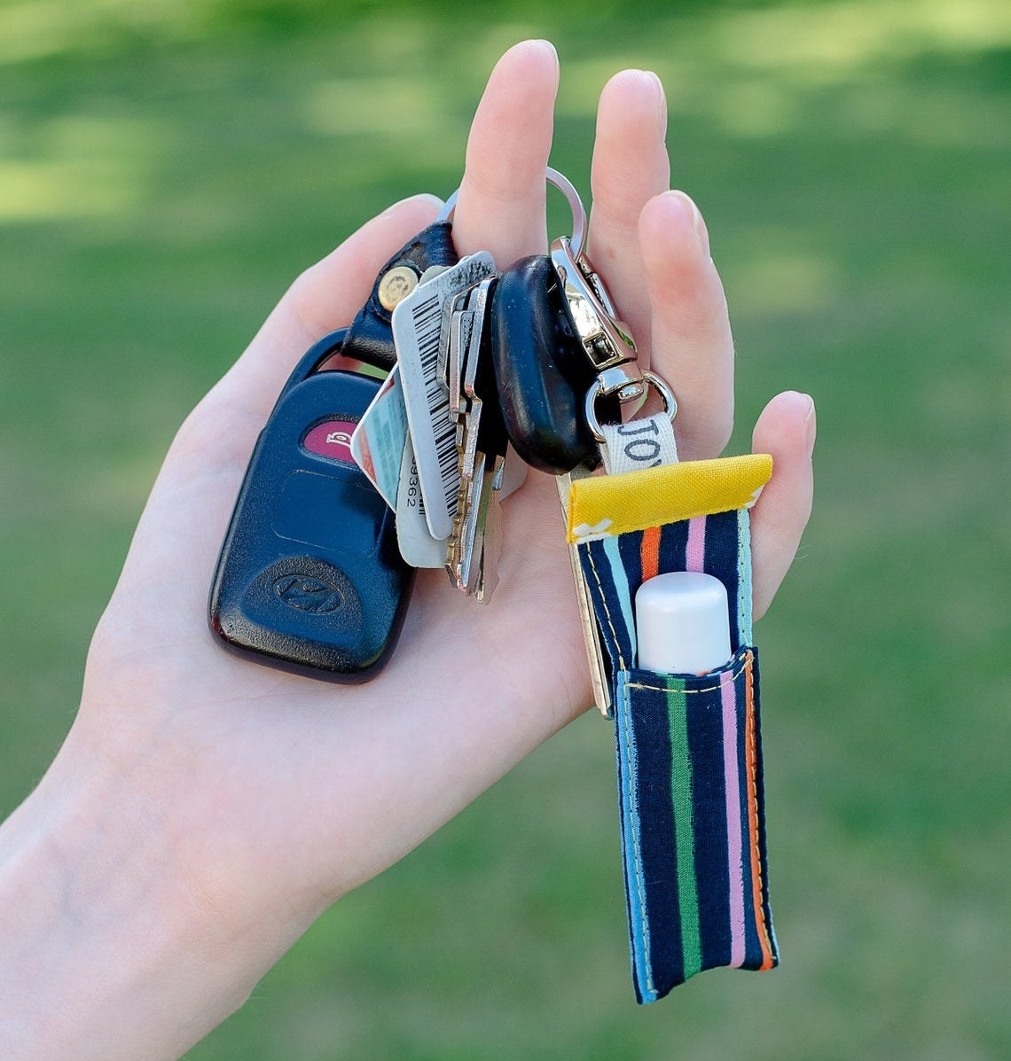 A person holding a keychain with the lip balm pouch on it