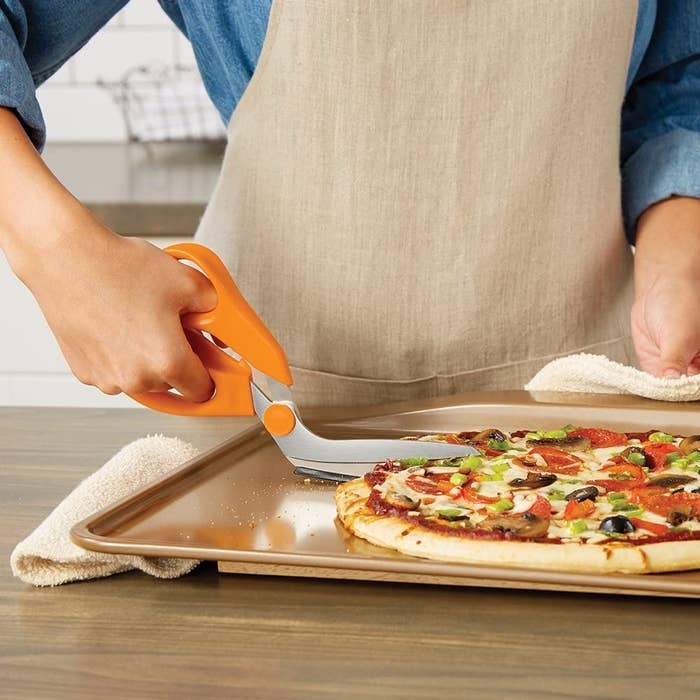 A person cutting a pizza with the scissors