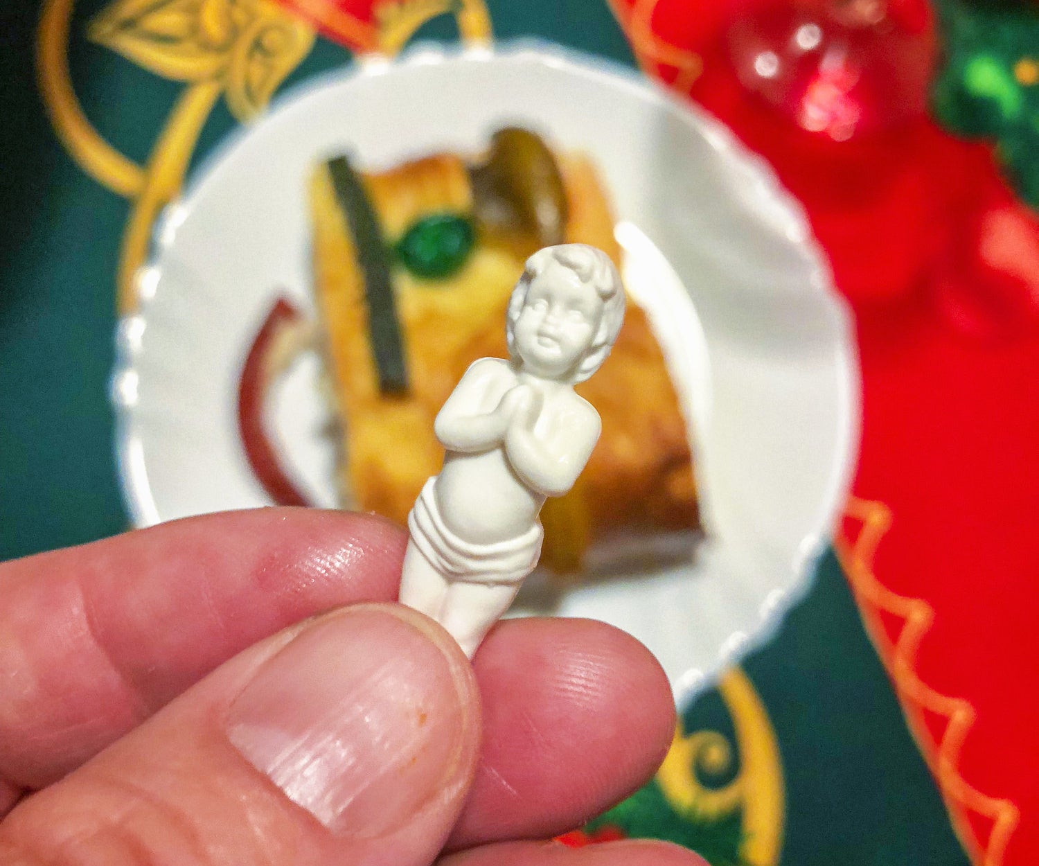A hand holding a white baby Jesus figure with a slice of Rosca in the background 