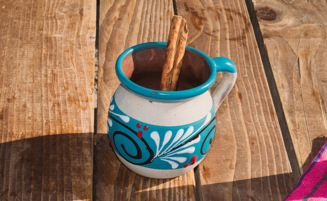 A close-up photo of a mug of champurrado with a cinnamon stick inside of it