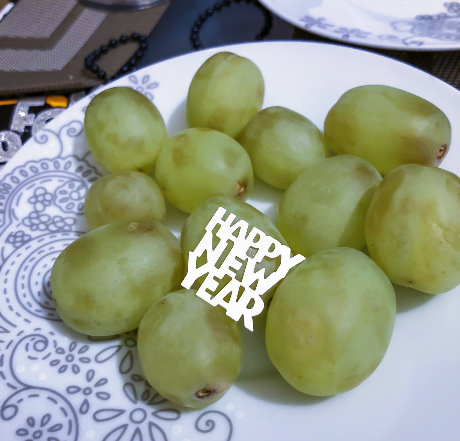 A photo of a dozen green grapes on a plate with a Happy New Year decoration on it