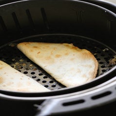 Two quesadillas in the basket of an air fryer.