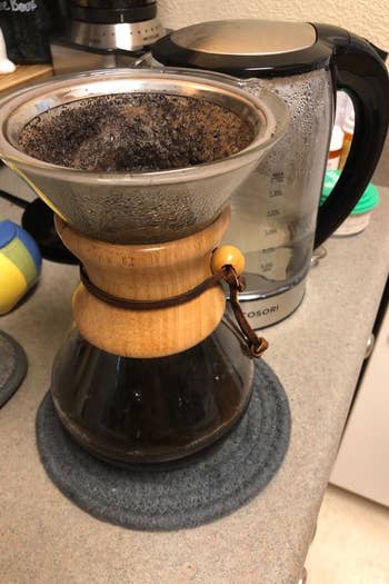 A reviewer photo of a glass pour-over coffee carafe with the reusable filter inserted in the top filled with coffee grounds and water 