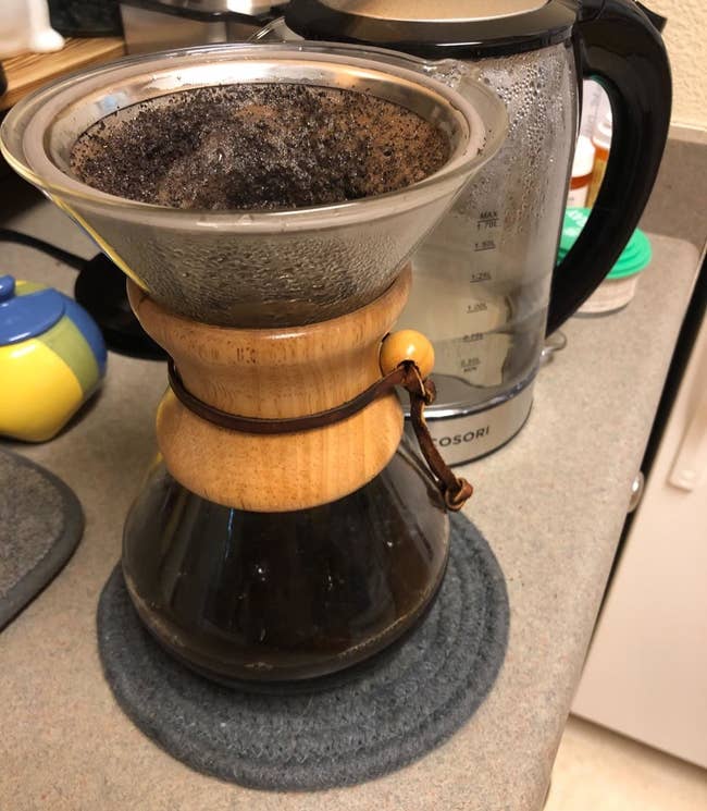 A reviewer photo of a glass pour-over coffee carafe with the reusable filter inserted in the top filled with coffee grounds and water 