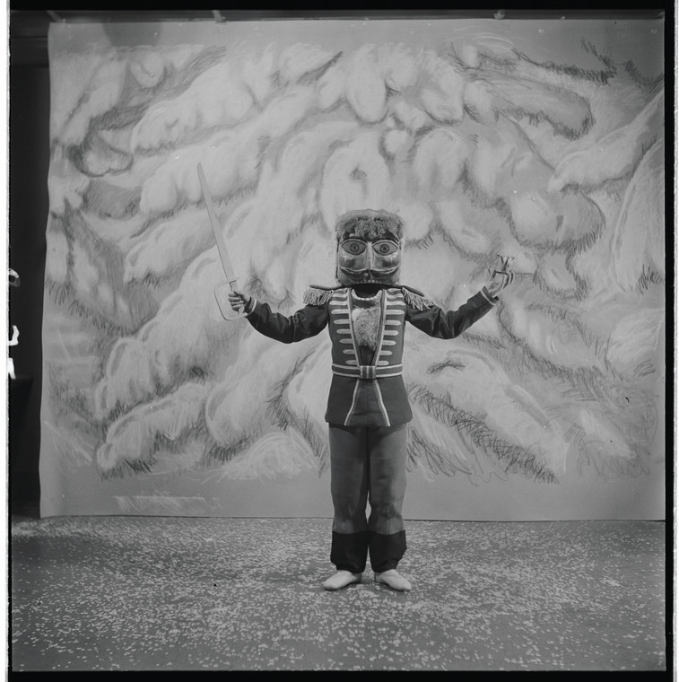 A boy in the Nutcracker costume holds a fake sword in front of a painted background