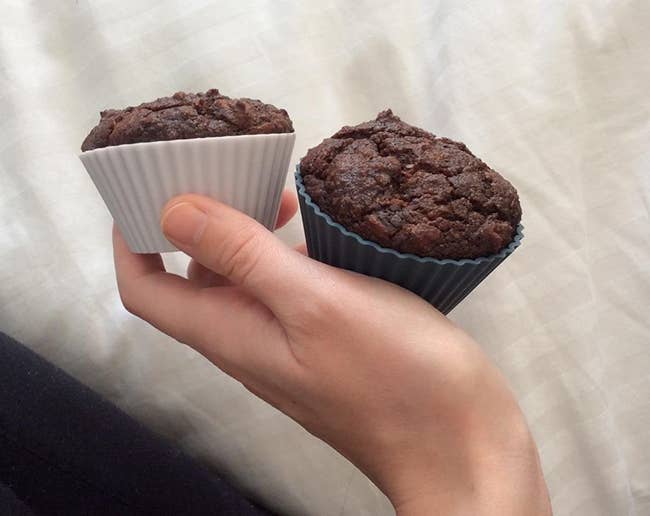 A reviewer photo of a hand holding two chocolate cupcakes that are in the silicone baking cups 