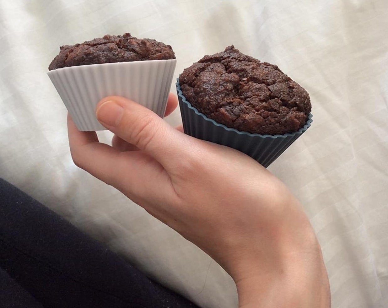 A reviewer photo of a hand holding two chocolate cupcakes that are in the silicone baking cups 