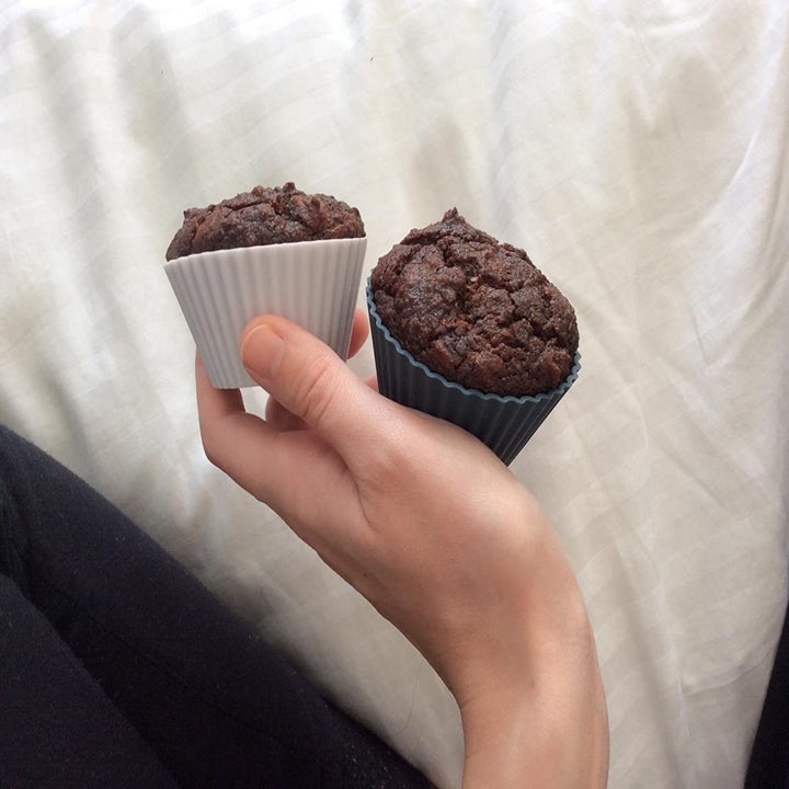 A reviewer photo of a hand holding two chocolate cupcakes that are in the silicone baking cups