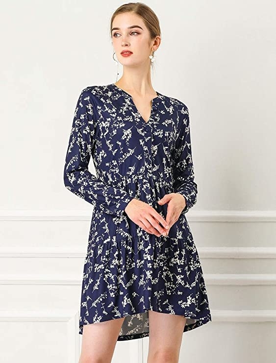 A model wearing the slightly high-low, tiered, long sleeve mini dress with button detail V-neckline in navy and white