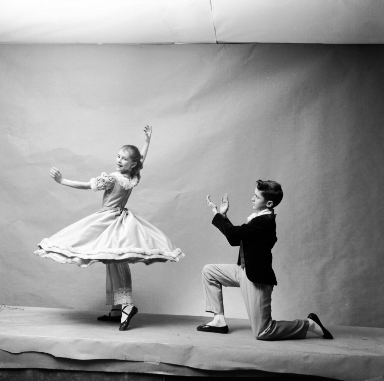 A girl ina dress twirls and a boy kneels and claps beside her in a studio photo shoot