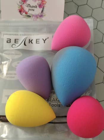 reviewer's five tear-drop shaped makeup sponges in different sizes and colors 