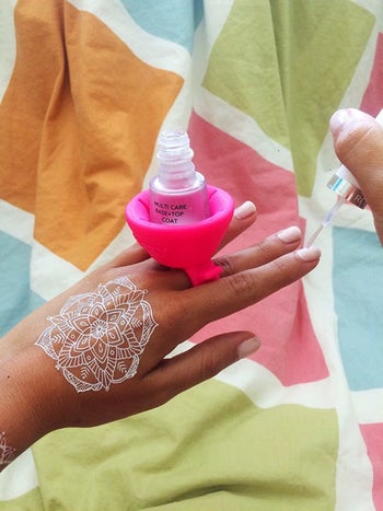 A pink silicone ring that covers two fingers and secures a bottle of nail polish upright 