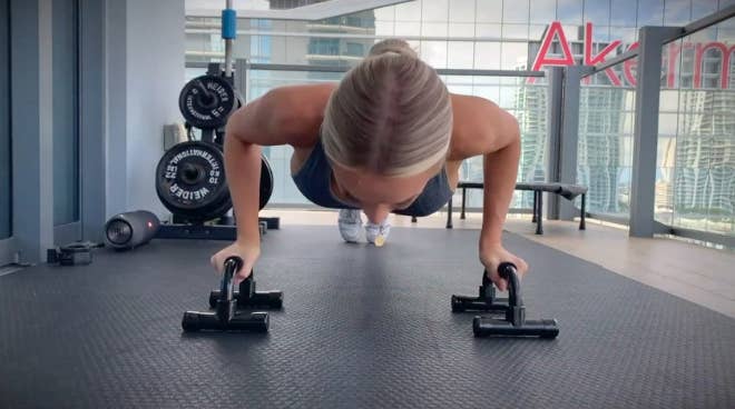 Model goes down in push-up position while holding black push-up handle bars on floor