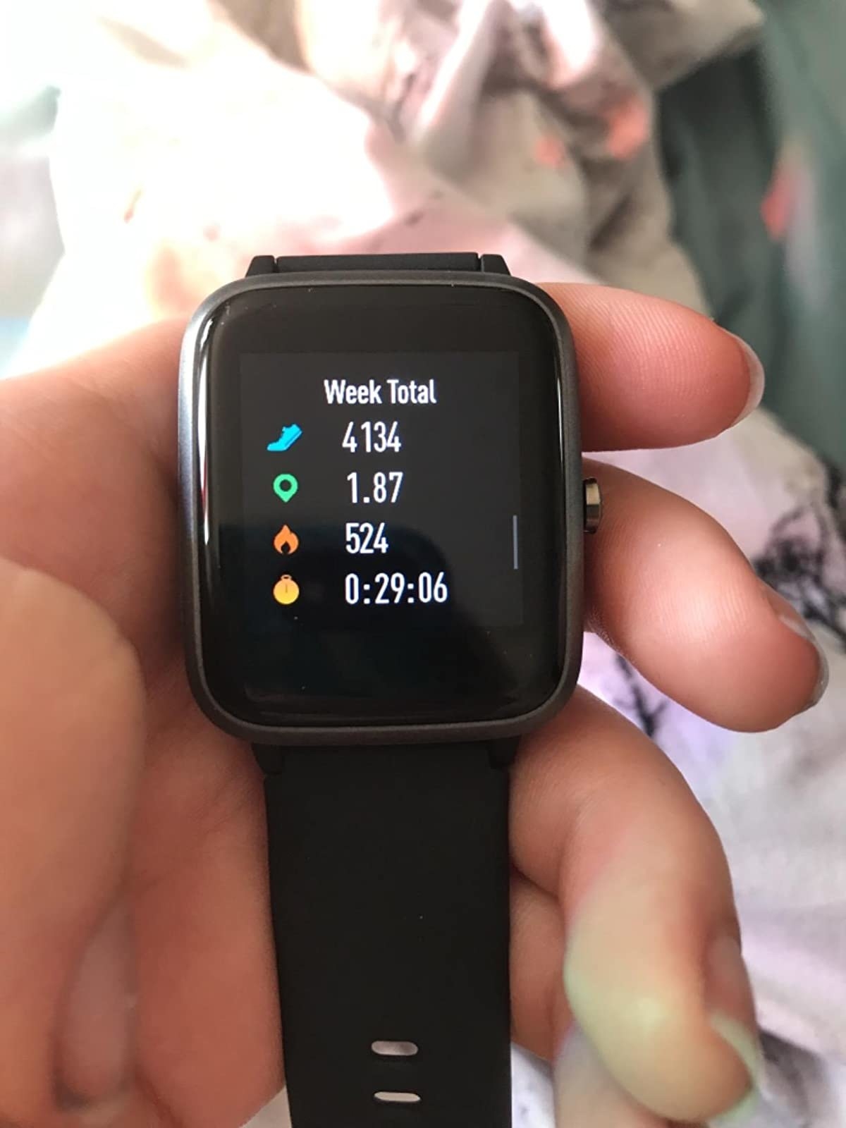 Reviewer holds black fitness tracker that shows steps walked, miles walked, calories burned, and time of workout on a watch-like screen