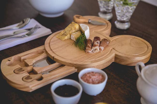 the wooden mickey-shaped cheese board with a drawer out filled with cheese knives