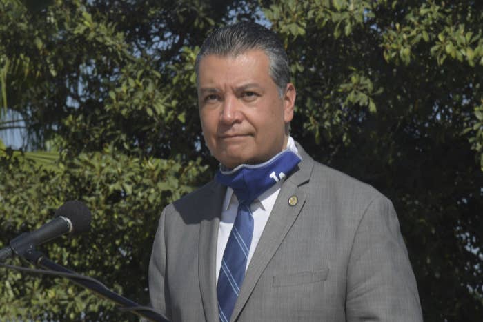 Alex Padilla stands outside, wearing a grey suit and an LA Dodgers face mask