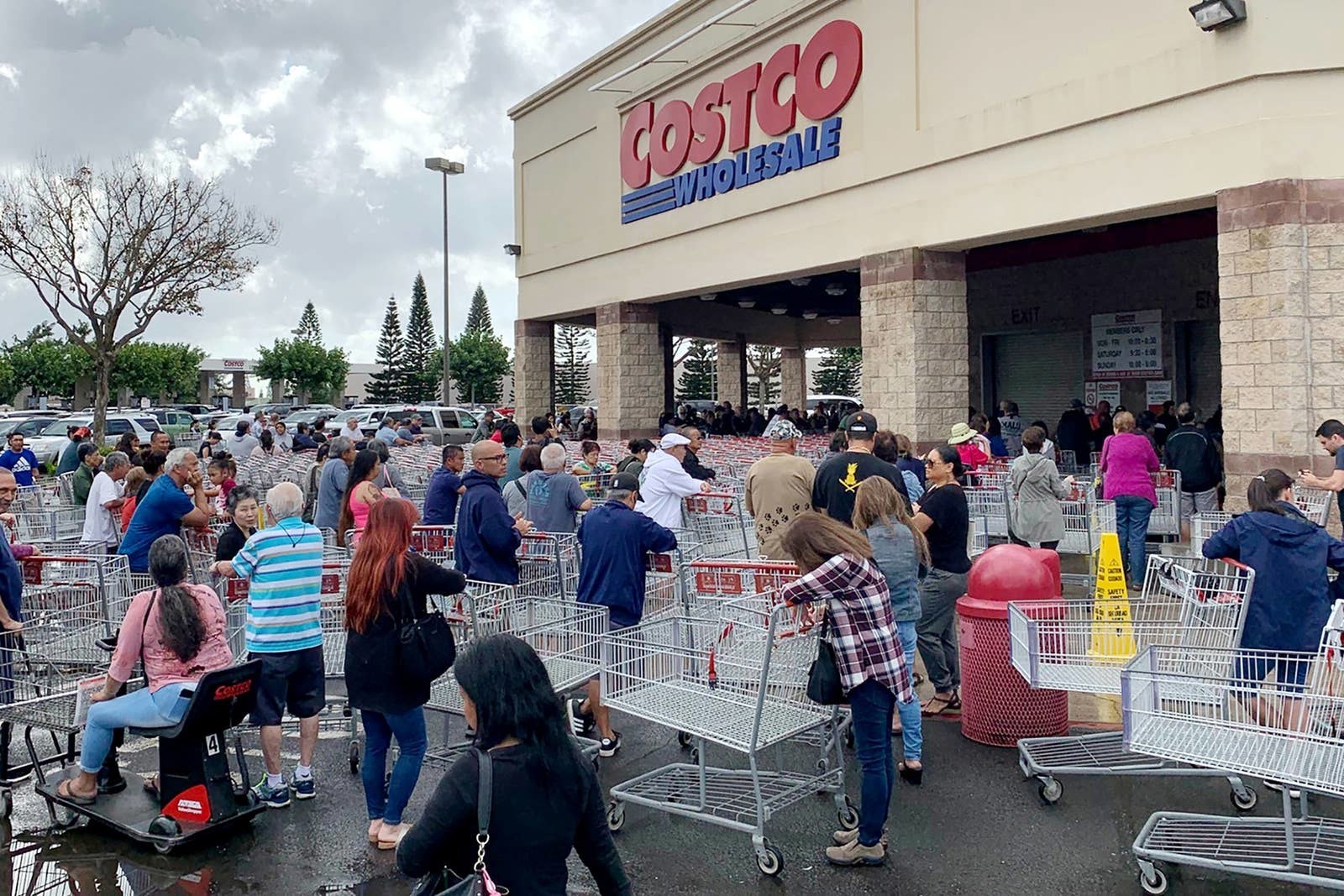 Shoppers with empty carts stand in a disorganized group outside a Costco