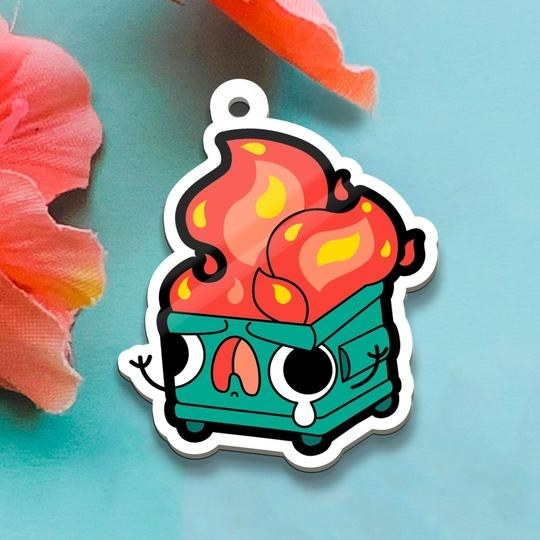 The charm featuring a cartoon dumpster on fire with a screaming face