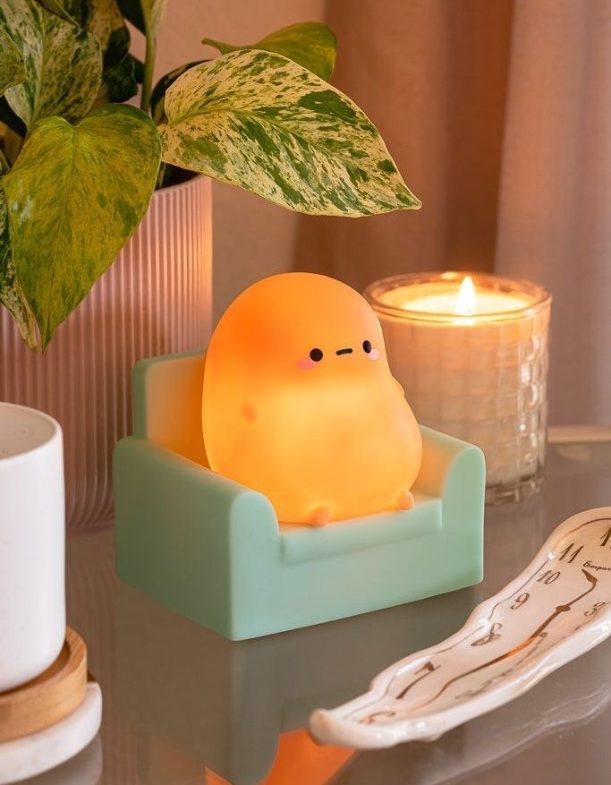 The small light shaped like a potato with a face, arms, and legs on a green armchair