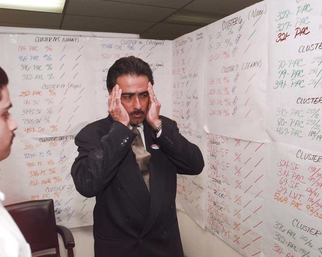 A man clutching his temples as he looks at figures and numbers taped to a wall