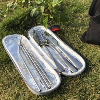 The same felted container opened to reveal a stainless steel fork, knife, spoon, two straws, a pair of chopsticks, and a spoon straw brush