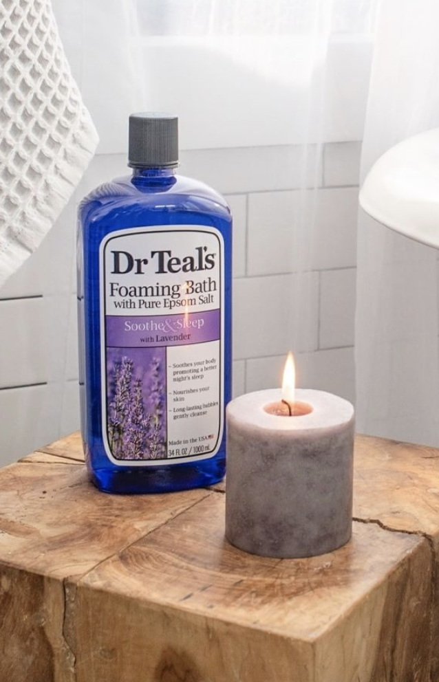 the bottle of Dr Teals on a wood block next to a candle