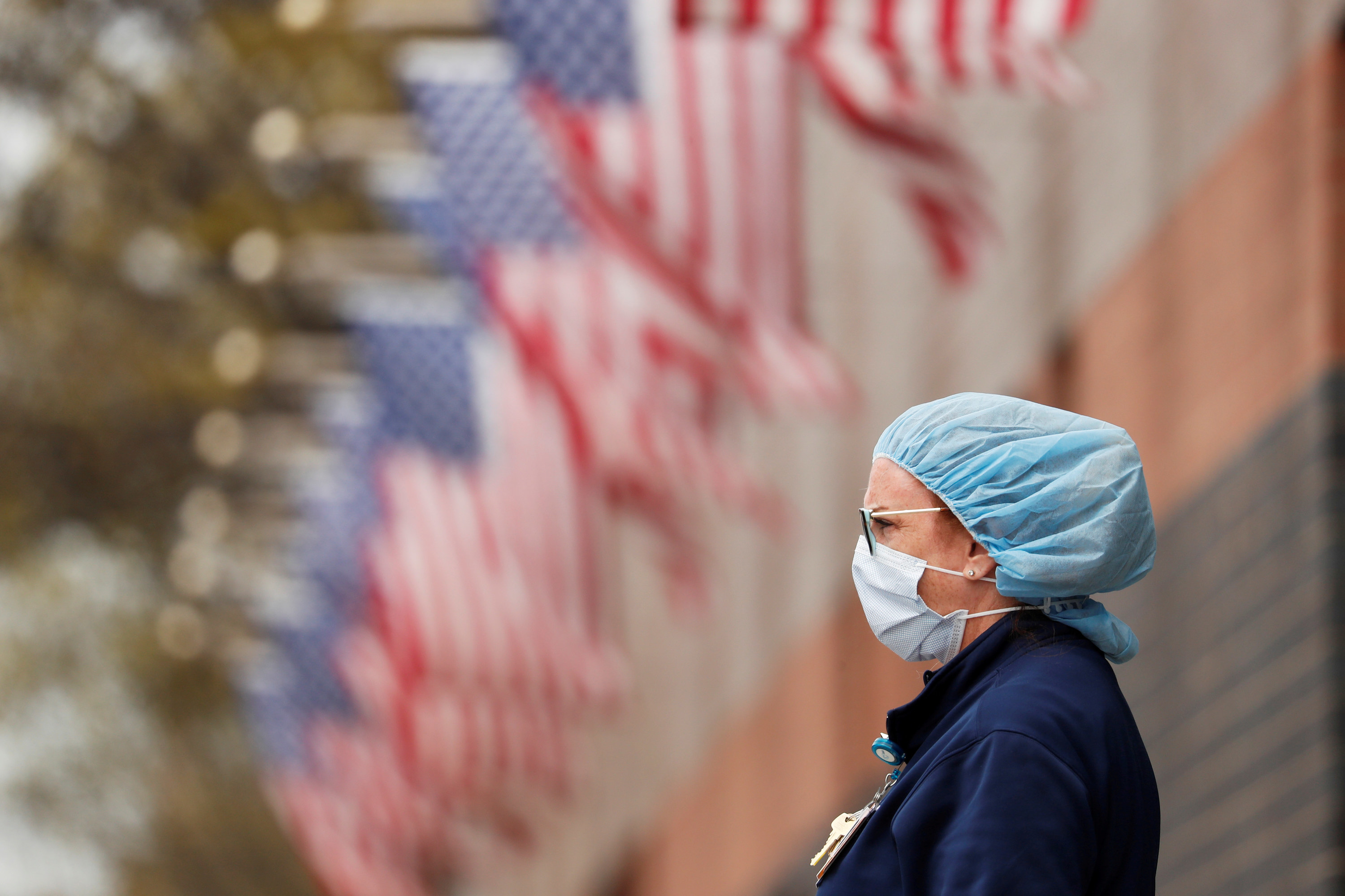 A nurse wearing PPE stands in front of American flags