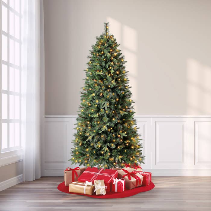 artificial christmas tree lit up with clear lights and wrapped presents underneath the tree