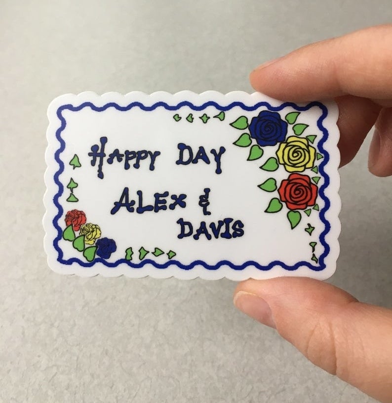 A sticker shaped like the "Happy Day Alex & Davis" cake from the show