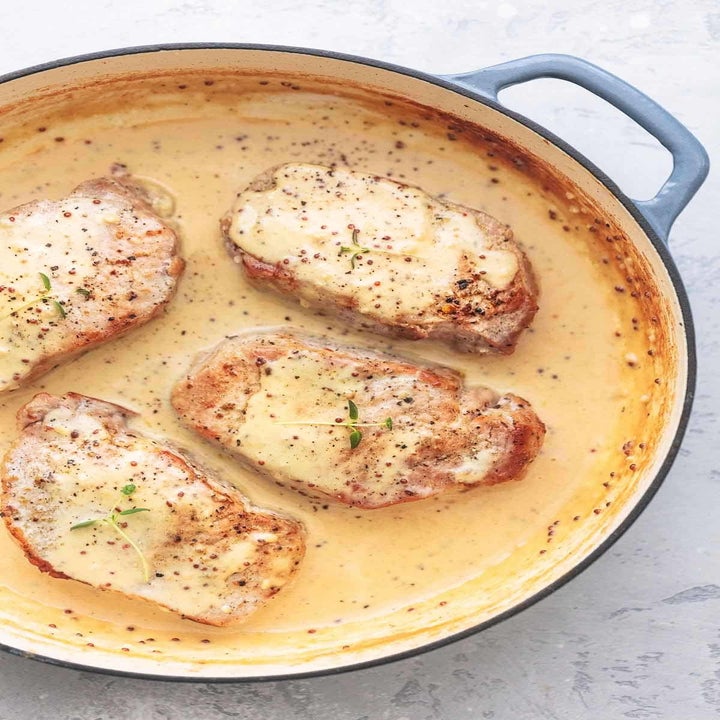 Four pork chops in Dijon cream sauce in a pan.