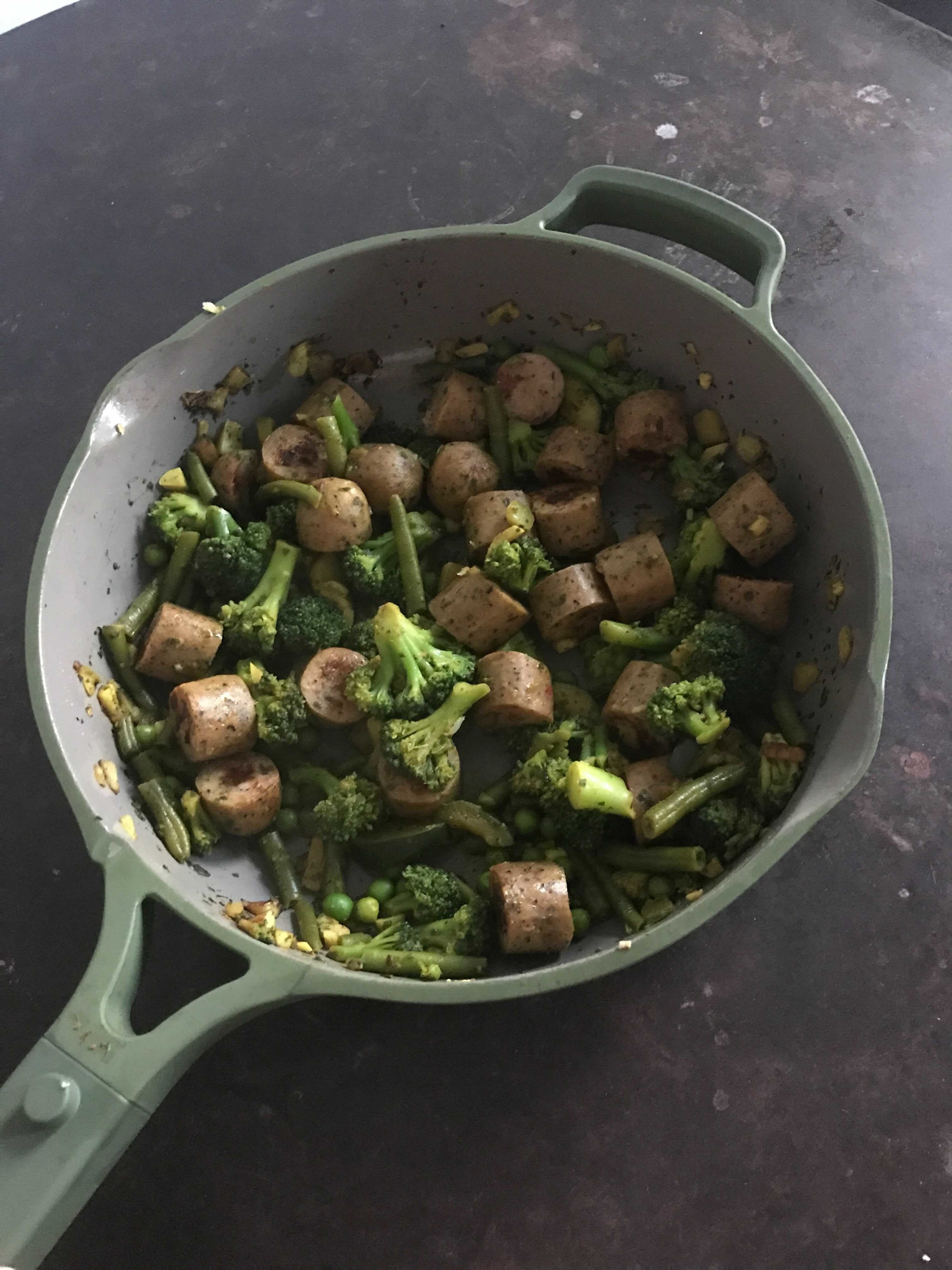 The pan in green with sausage and veggies inside