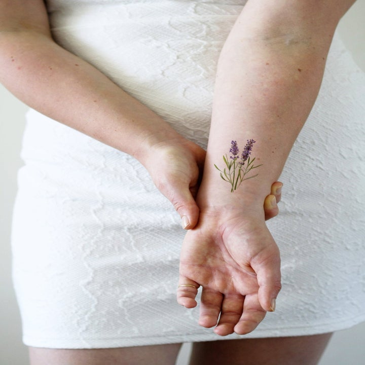 A model's wrist with a lavender flower  tattoo on it 