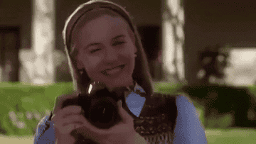 cher from Clueless smiling and taking a photo with her camera 