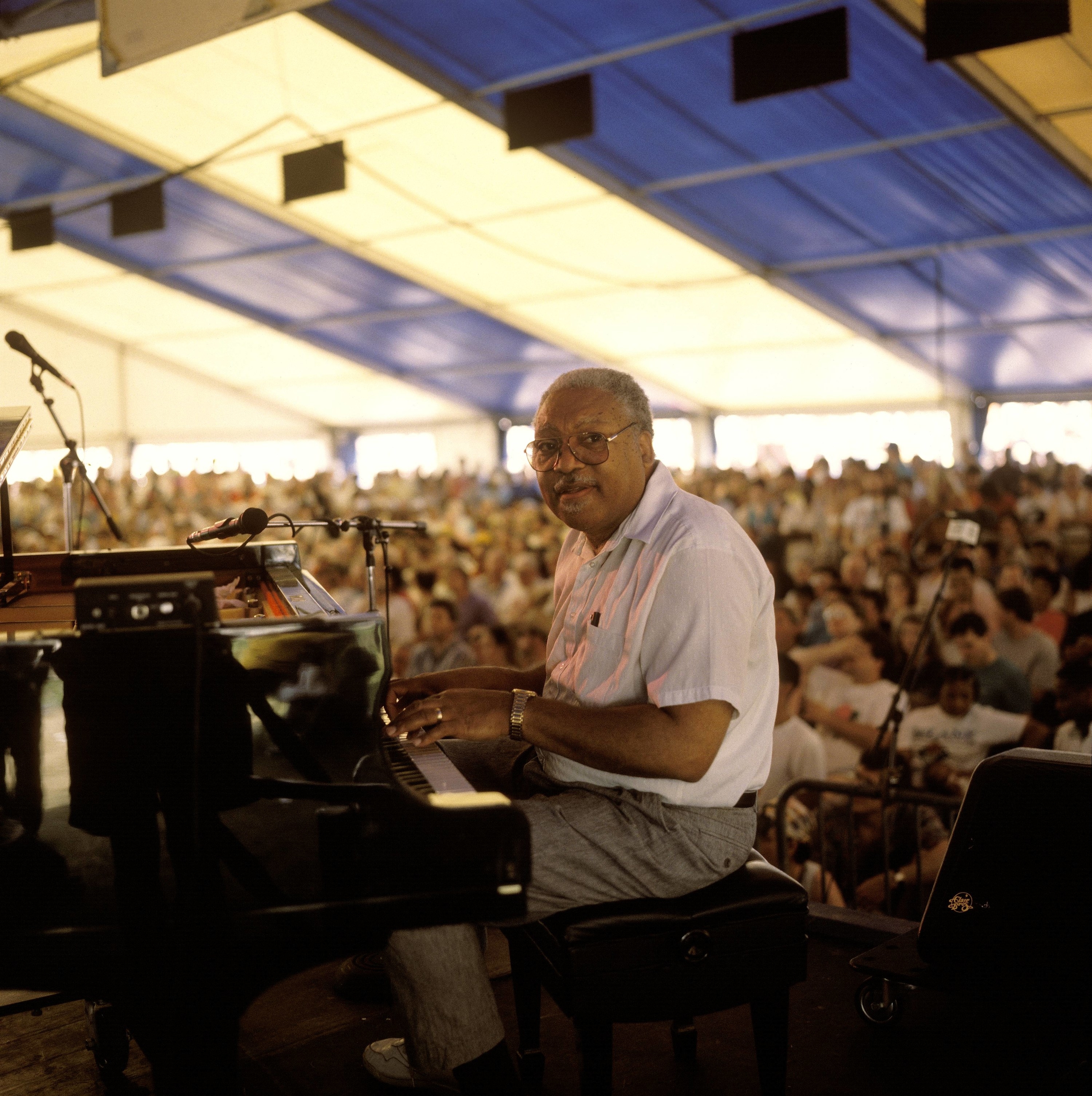 Man at a piano on stage with a crowd behind him