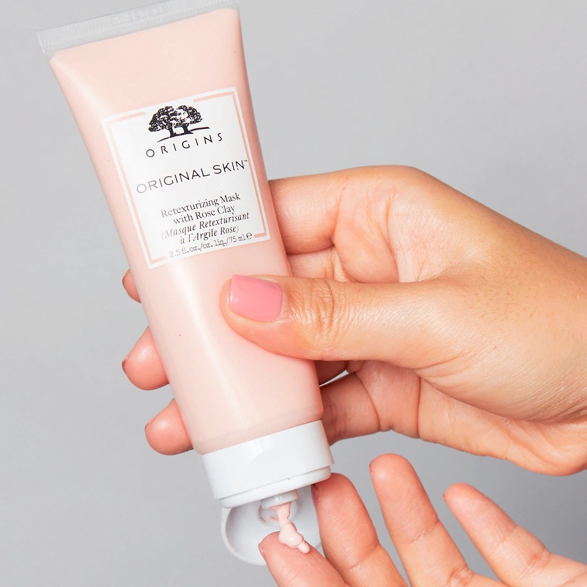 A model holding the face mask tube and squirting some of the pink lotion onto a finger