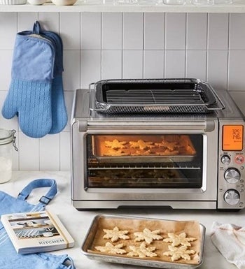 the toaster oven on a counter near a tray of cookies