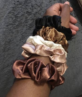 Reviewer with six scrunchies in neutral tones on their arm 