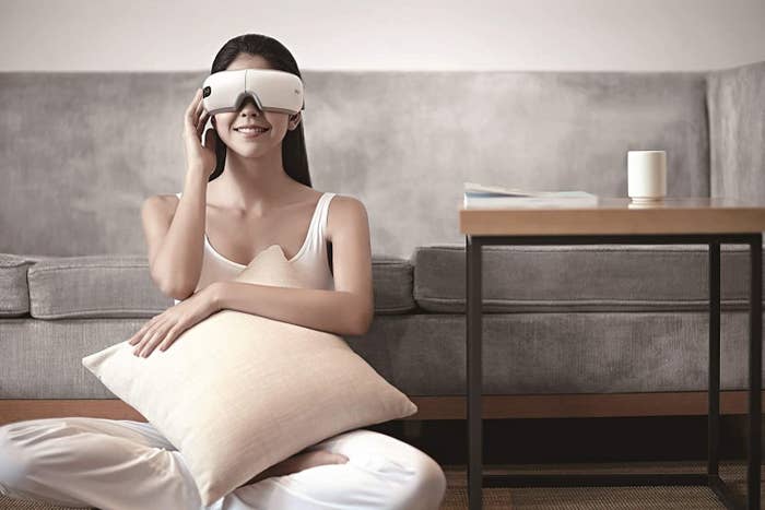 A person wearing the eye massager and sitting in front of a sofa.