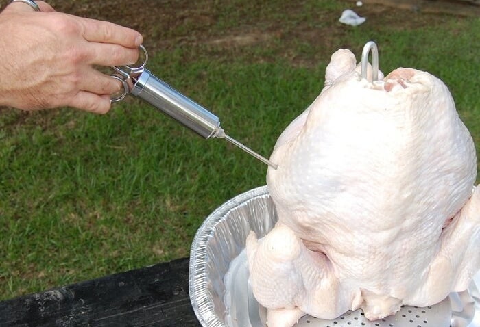 White hand injecting seasoning into a chicken