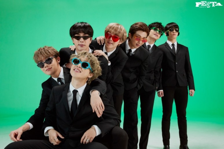 The BTS members wear suits and quirky sunglasses while posing in a row