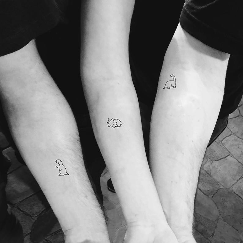 Three forearms with mini dinosaur tattoos drawn in the same minimalist style