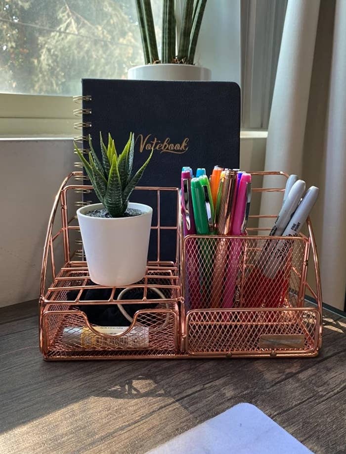 reviewer image of the rose gold desk organizer in the corner of a customer's desk holding a small succulent, pens, and a notebook”class=