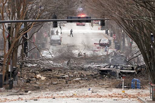 Debris from an exploded RV, including burned-out cars and fallen tree limbs, litters a snowy street