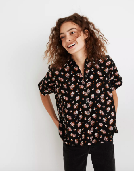 Model wearing boxy black button up shirt with pink floral motif on it 