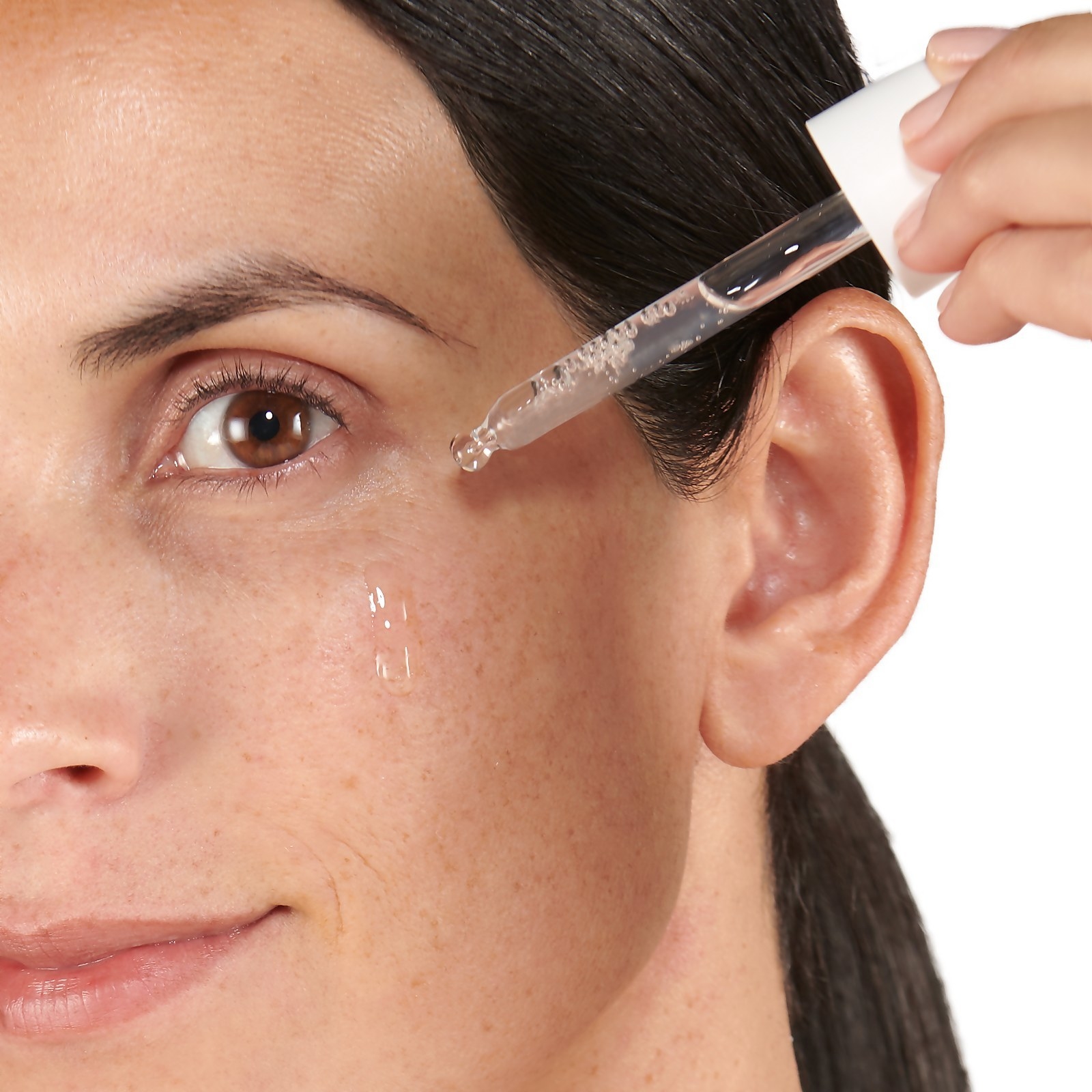 Model applying the clear product to their cheek with a dropper