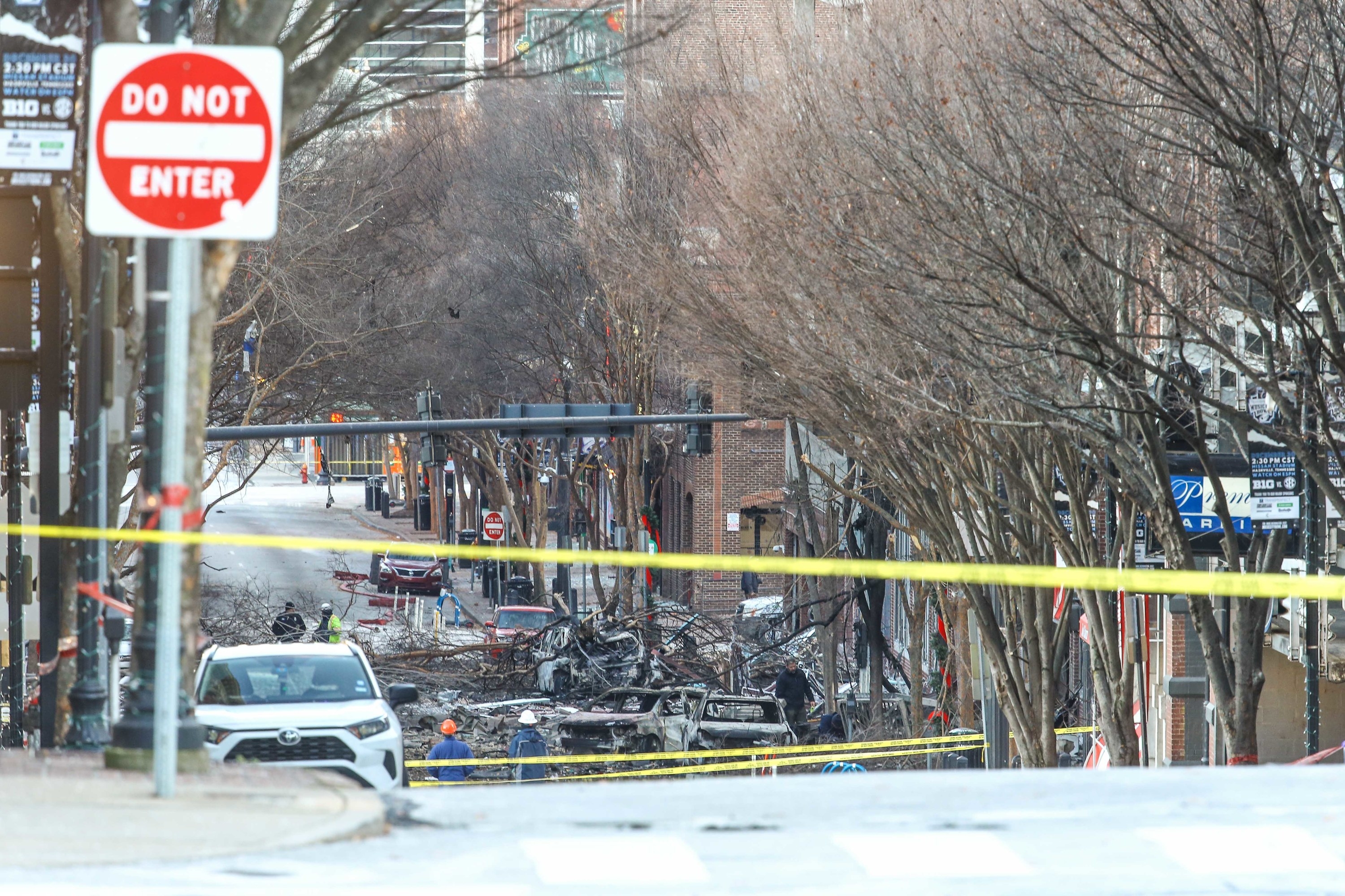 Police tape crosses off an area where debris from an explosion litters the street, including fallen tree branches and burned-out cars